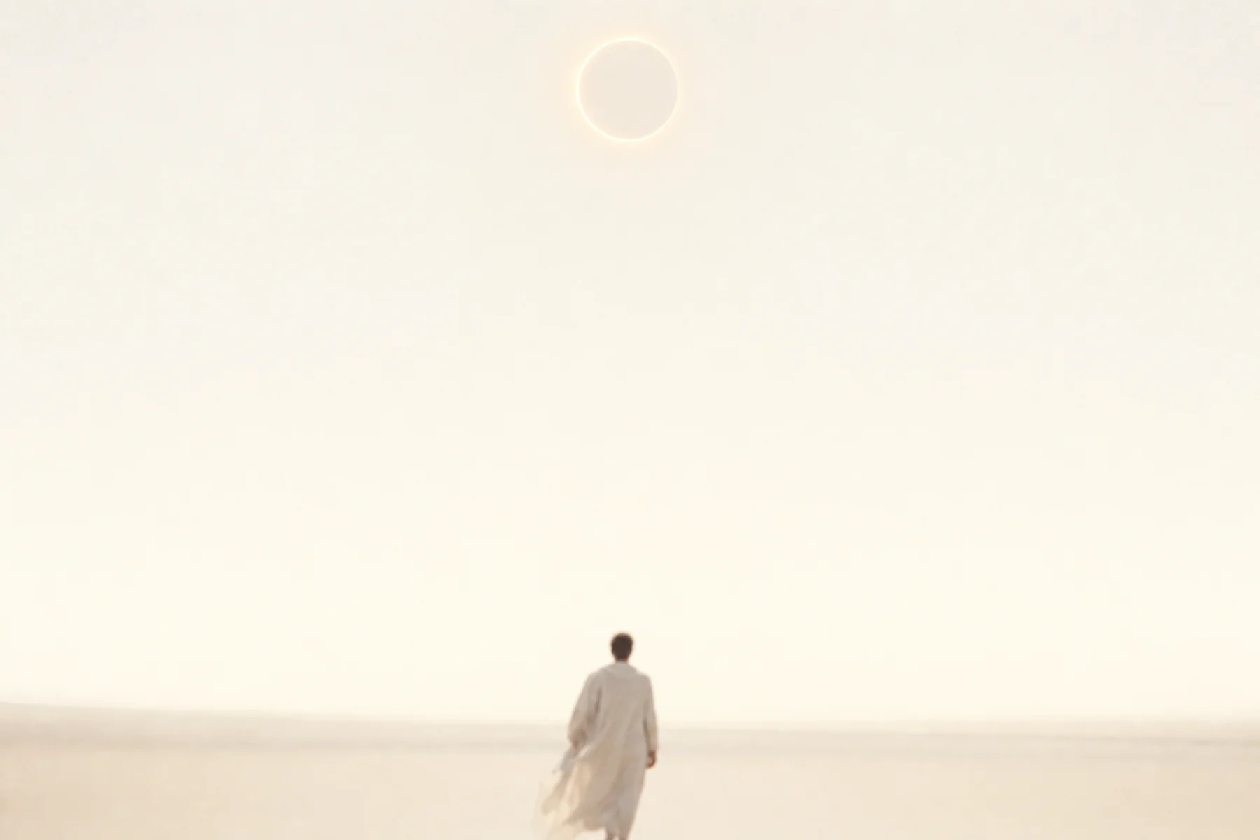 Un cielo de marfil al amanecer con un anillo de luz ámbar, y abajo la silueta difusa de un hombre vestido de lino claro caminando hacia la luz.